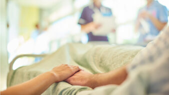 patient in a hospital bed holding hands with a visitor