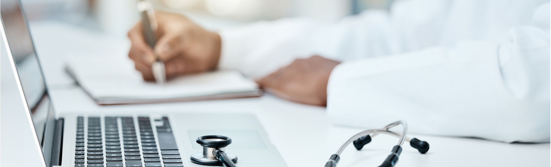 doctor writing in a notebook with computer on a desk
