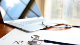 open laptop on top of prescription pad and stethoscope