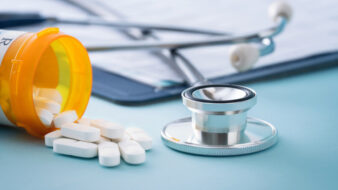 bottle of pills, clip board, and stethoscope on a doctors desk
