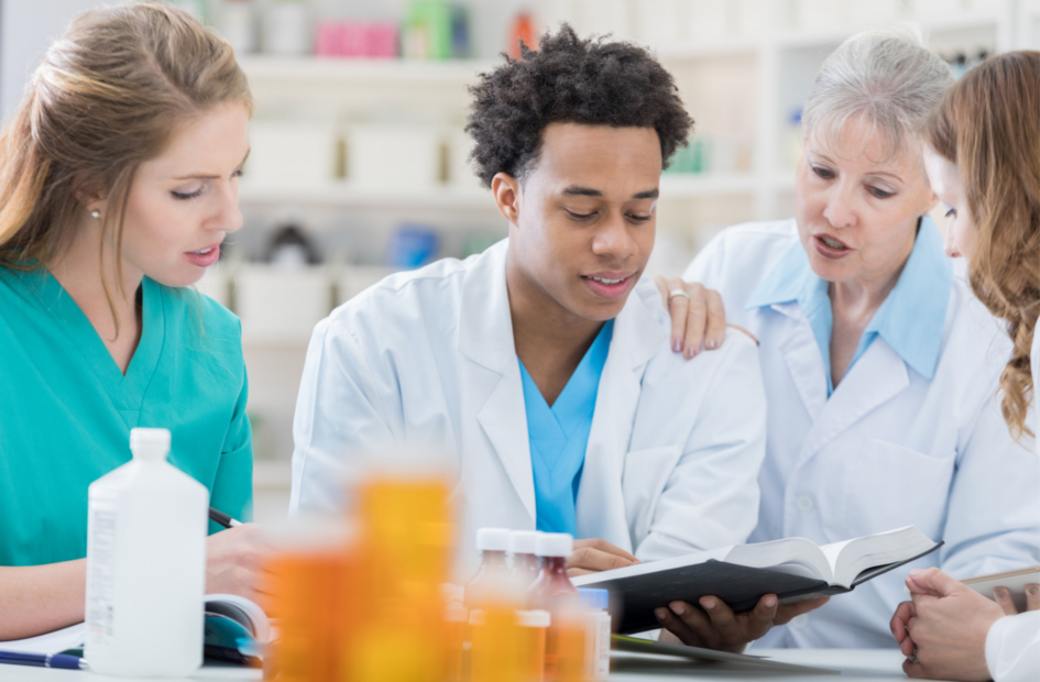 Two pharmacy technicians continuing education with a book and other pharmacists