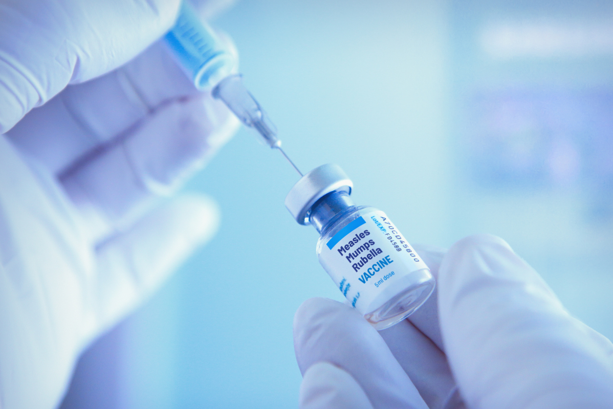 closeup of hands holding syringe and measles vaccine